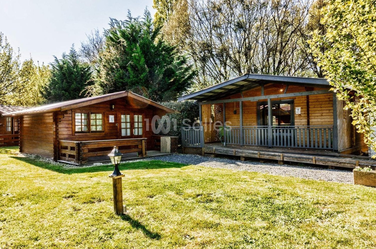 Deux chalets en bois entourés de verdure, avec une pelouse et des arbres en arrière-plan.