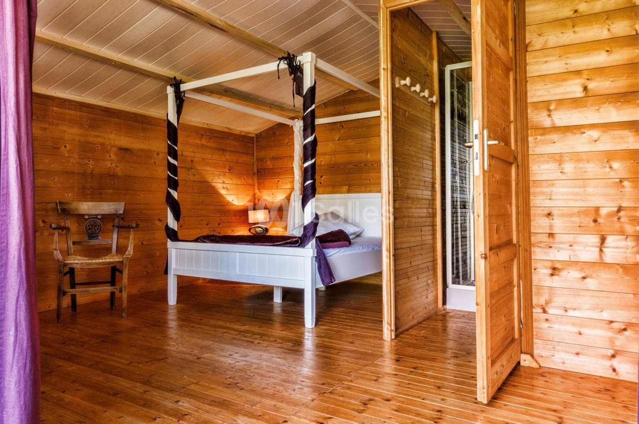 Chambre en bois avec lit à baldaquin blanc, rideaux violets, chaise en bois et lumière douce.