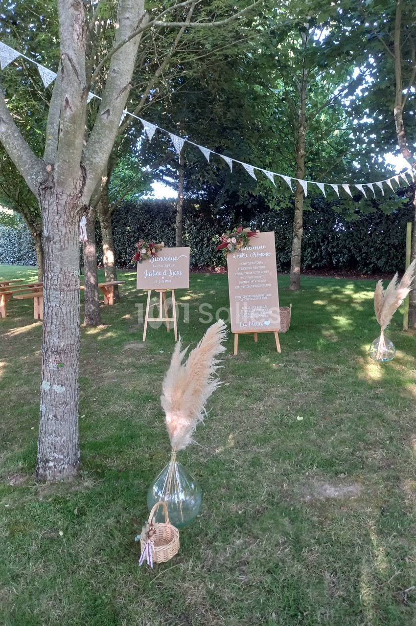 Décoration de mariage en plein air avec panneaux en bois, guirlandes de fanions et herbes de la pampa sous des arbres.