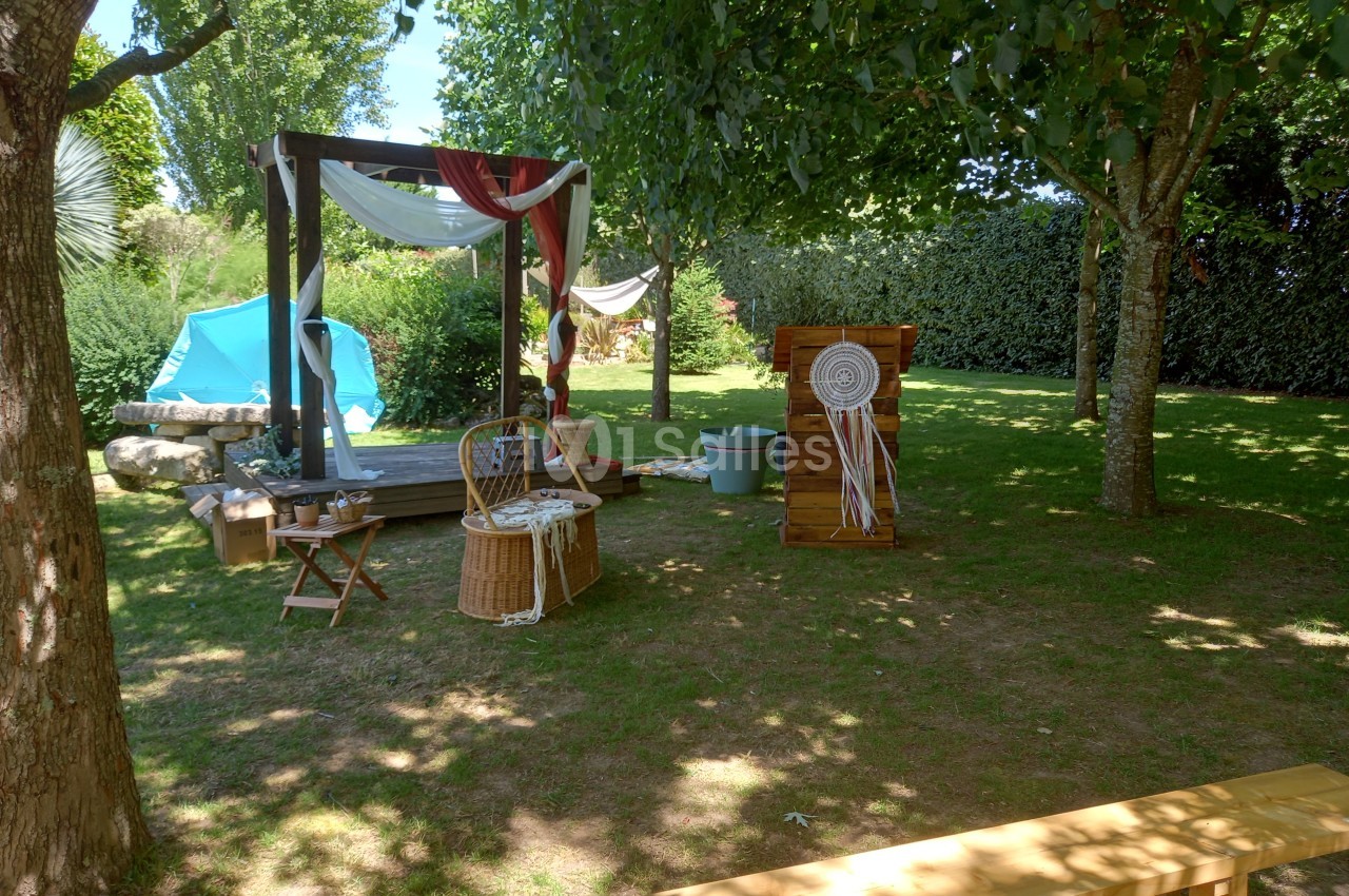 Espace extérieur ombragé avec arche décorée, chaises en bois, panier en osier et éléments de décoration bohème.