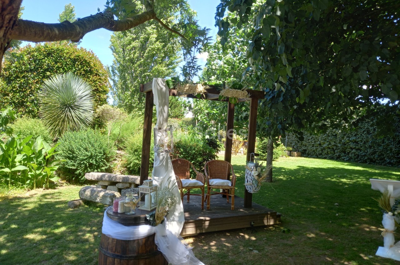 Pergola en bois décorée pour une cérémonie en plein air, entourée de verdure et d'éléments naturels.