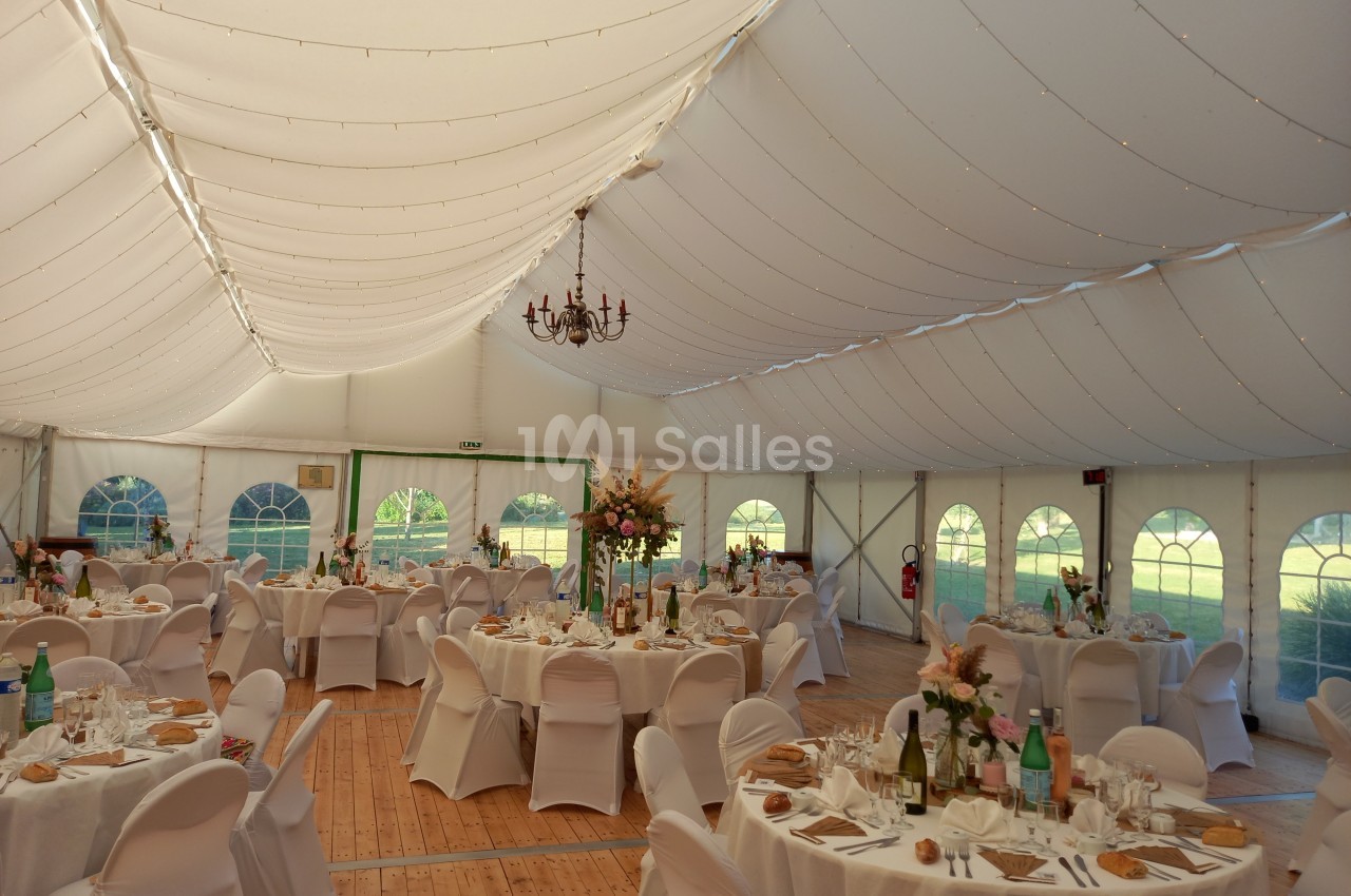 Intérieur d'une tente de réception décorée, avec tables rondes dressées et éclairage doux.