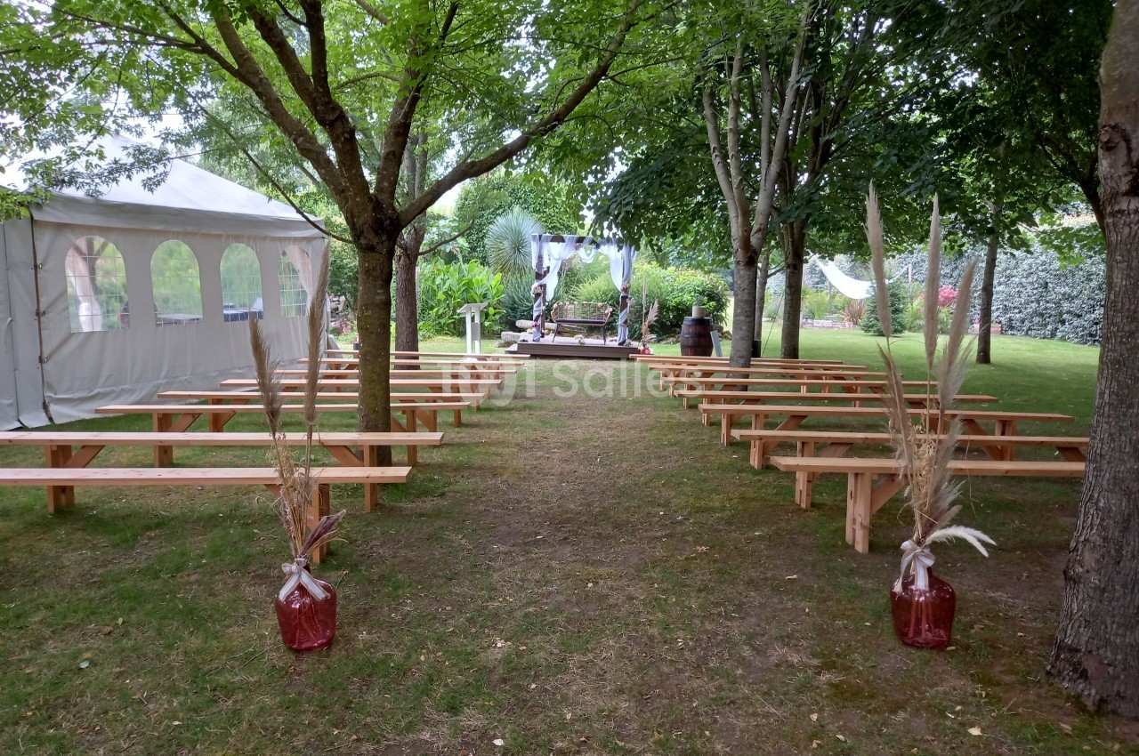 Allée centrale bordée de bancs en bois menant à une arche décorée, installée dans un jardin avec des arbres.