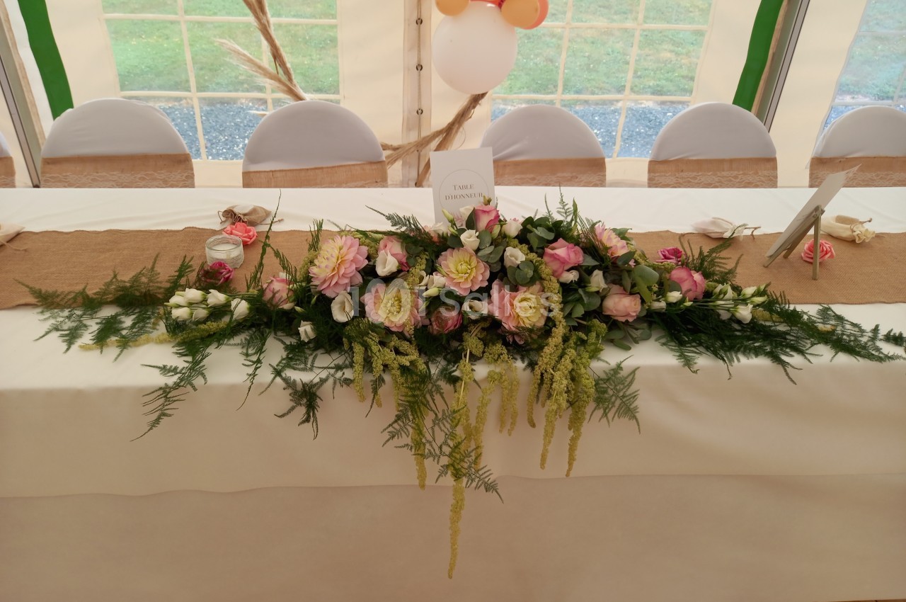 Décoration florale avec roses et feuillage sur une table blanche dans une salle de réception sous tente.