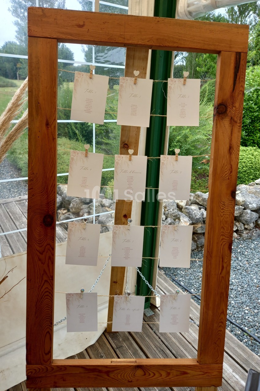 Cadre en bois vertical avec des cartes suspendues, affichant des noms ou des informations, dans un décor extérieur.