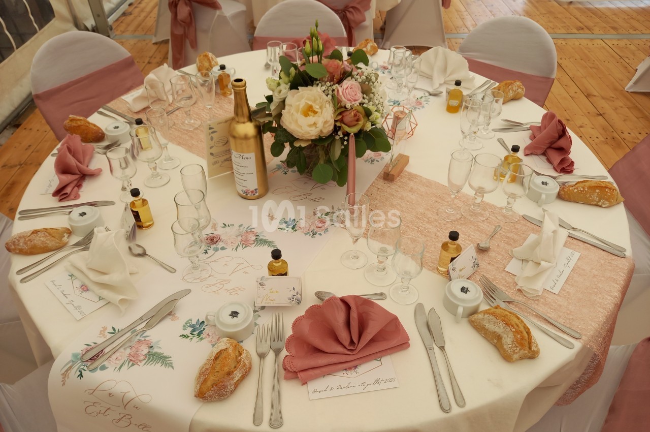 Table de mariage décorée avec nappe blanche, fleurs au centre, couverts, petits pains et bouteilles miniatures.