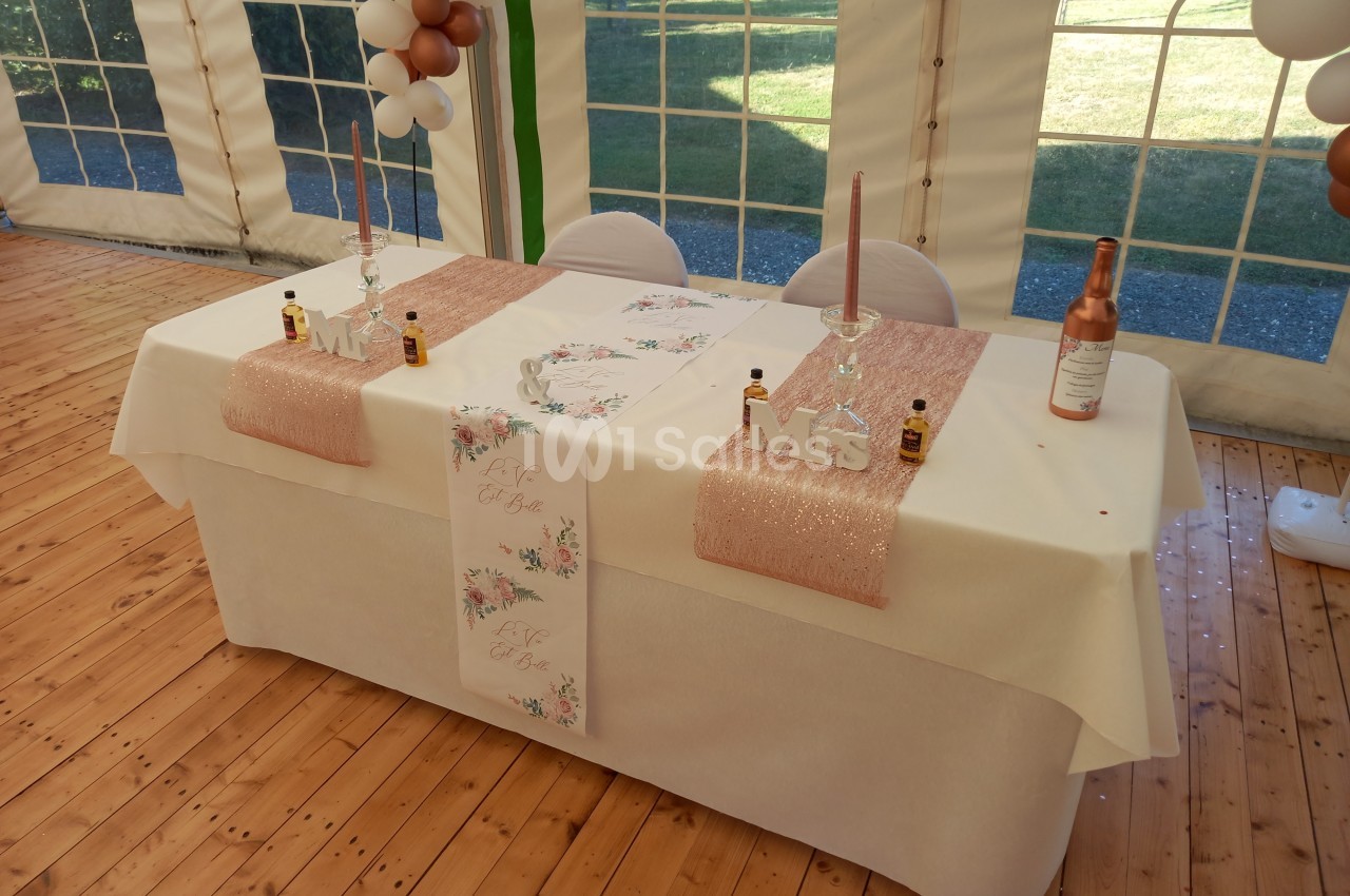 Table décorée pour un mariage avec nappes blanches, chemins de table roses, bougies et accessoires ’Mr & Mrs’.