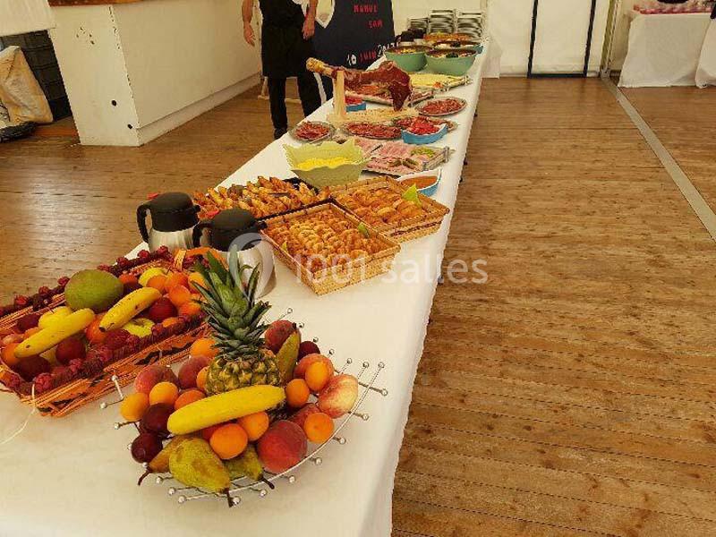 Table garnie de fruits, viennoiseries, charcuteries et plats variés dans une salle au sol en bois.