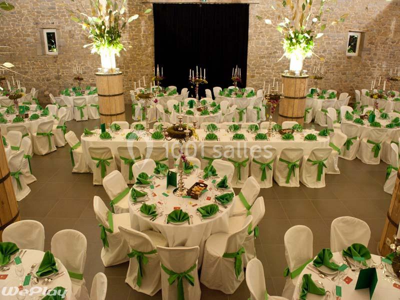 Salle de réception décorée avec des tables rondes et rectangulaires, nappes blanches et nœuds verts sur les chaises.