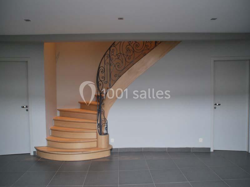 Escalier en bois avec rampe en fer forgé, situé entre deux portes blanches dans une pièce aux murs gris.
