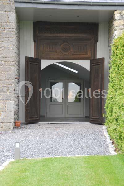 Entrée d'un bâtiment avec portes en bois ouvertes, encadrée de murs en pierre et donnant sur une porte vitrée.