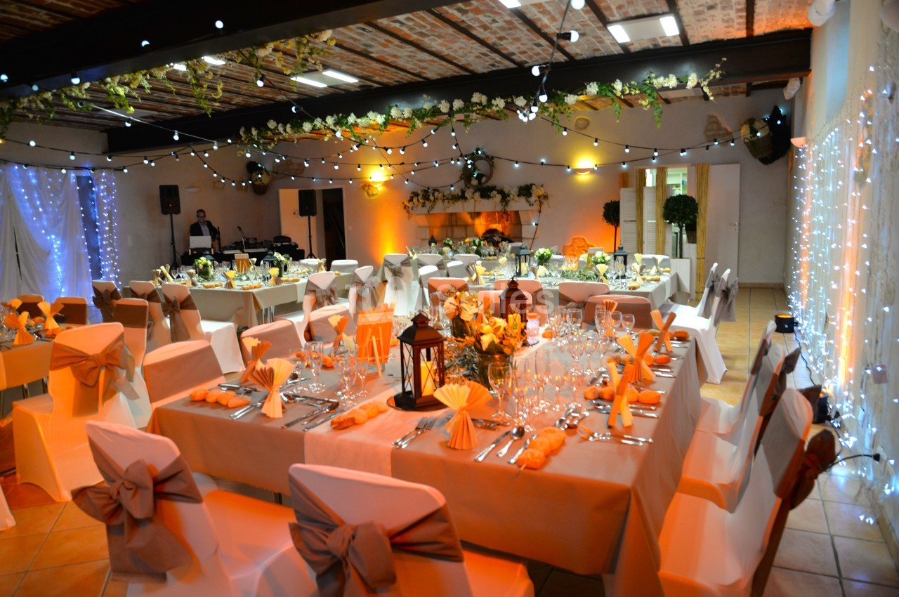 Salle de réception décorée avec des guirlandes lumineuses, des tables dressées et des chaises ornées de nœuds.