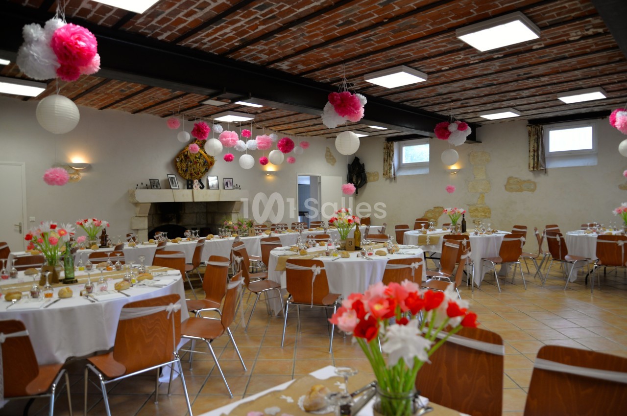Salle de réception décorée avec des tables rondes, nappes blanches, fleurs colorées et lanternes suspendues.