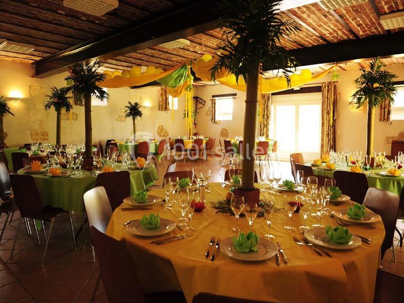 Salle de réception décorée avec des tables rondes dressées, nappes vertes et jaunes, et plantes en centre de table.