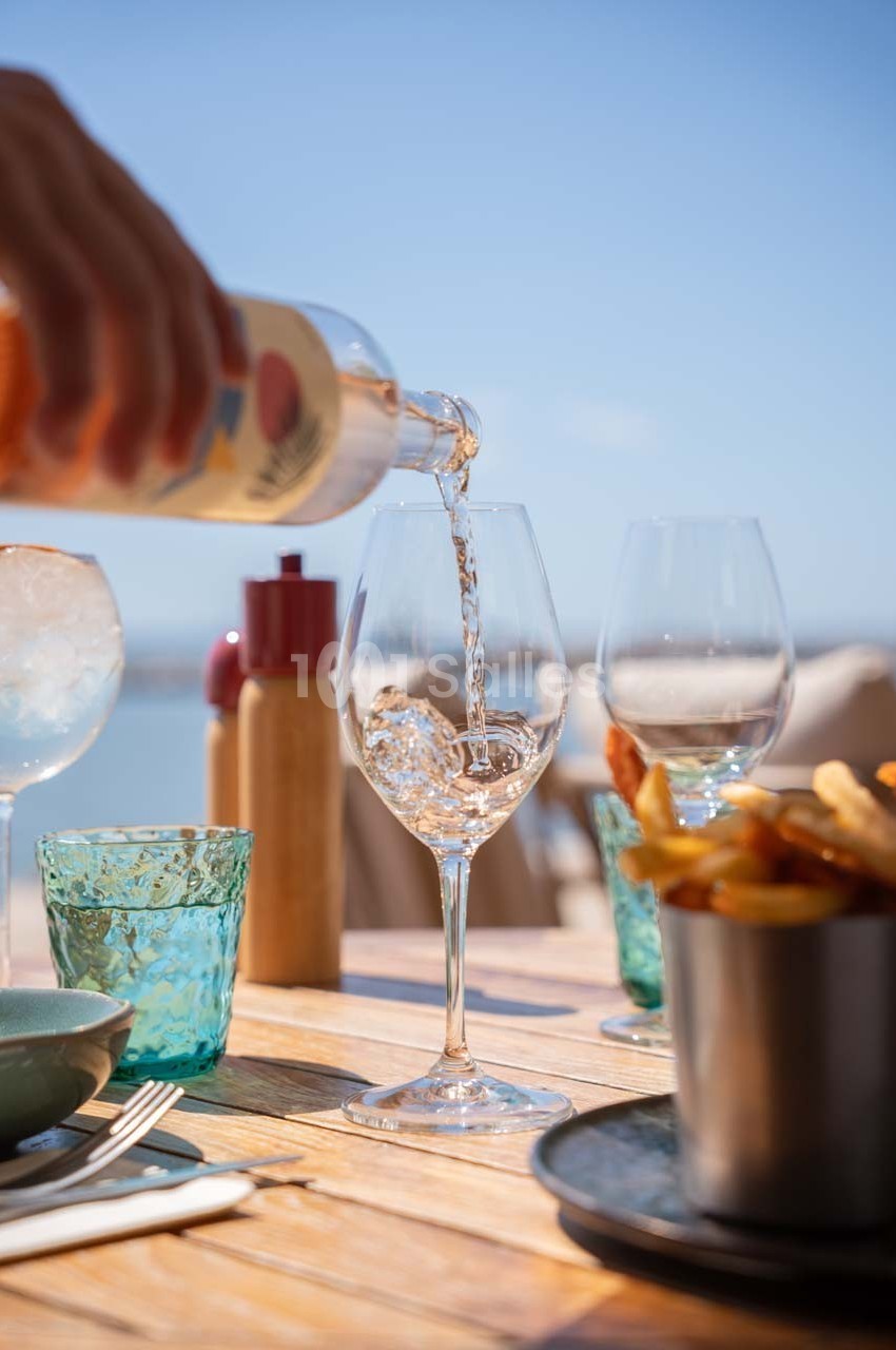 Un verre de vin rosé est servi sur une table en extérieur, avec des frites et des verres vides à proximité.