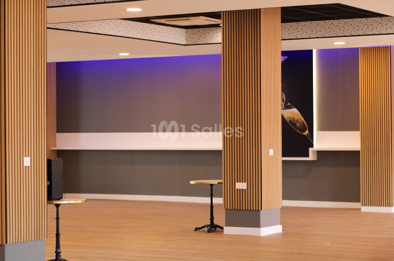 Salle vide avec parquet clair, colonnes en bois, murs gris et éclairage LED violet au plafond.