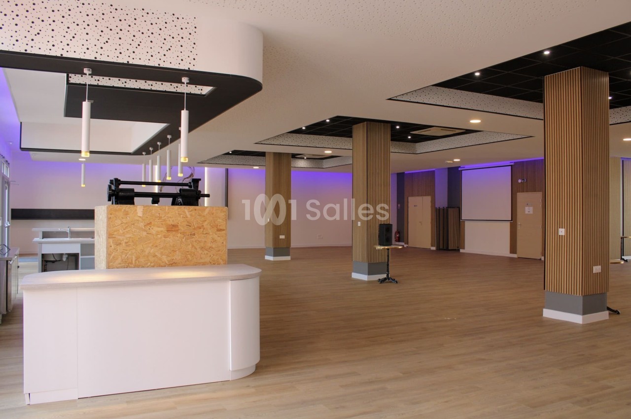 Salle moderne avec parquet, éclairage LED violet, colonnes en bois et comptoir blanc au premier plan.
