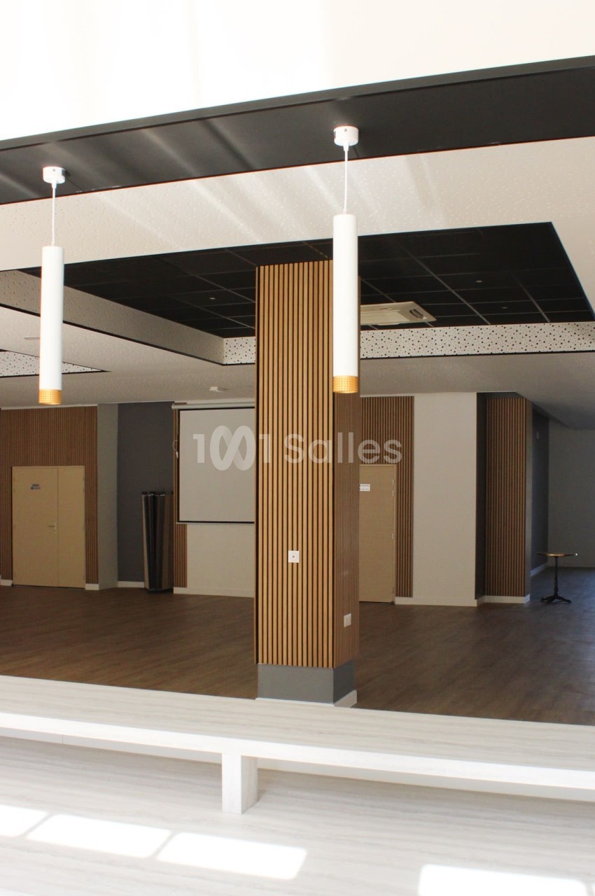 Salle moderne avec parquet, murs clairs, panneaux en bois vertical, plafond noir et éclairage suspendu.
