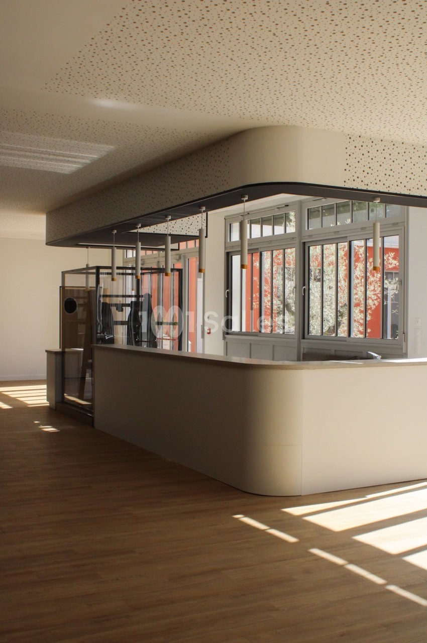 Comptoir moderne dans un espace lumineux avec parquet en bois et grandes fenêtres laissant entrer la lumière naturelle.