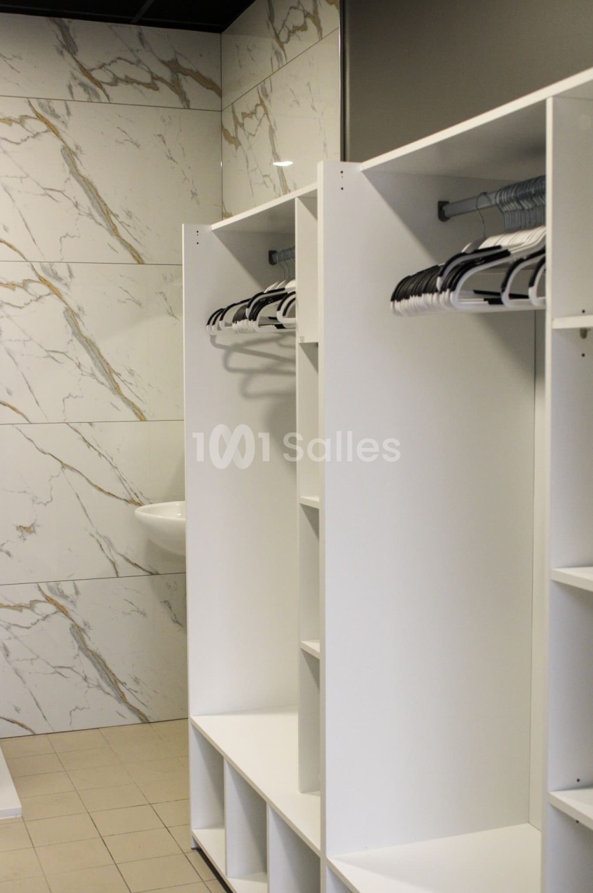 Vestiaire moderne avec casiers blancs ouverts, cintres suspendus et murs en carrelage effet marbre.
