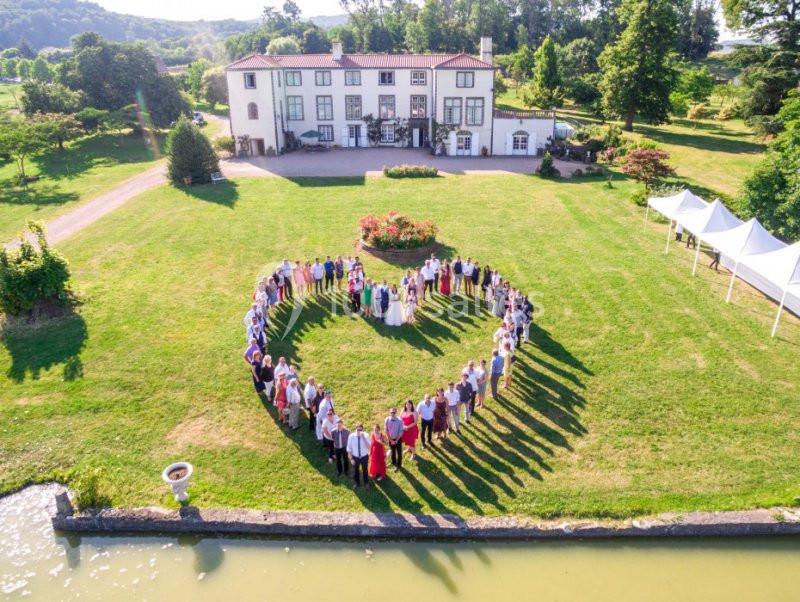 Un groupe de personnes formant un cœur sur une pelouse devant un grand bâtiment blanc entouré de verdure.