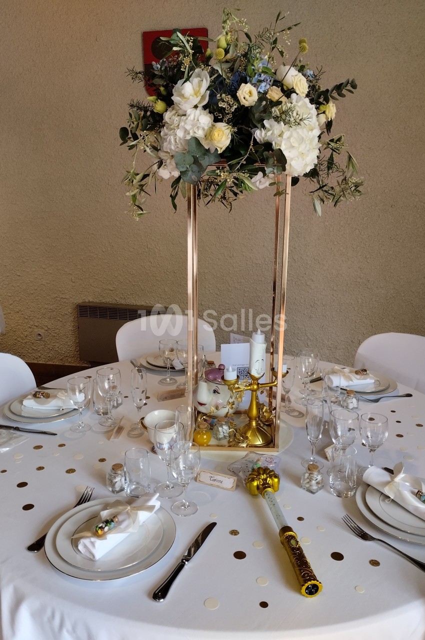 Table de réception décorée avec une composition florale surélevée, vaisselle élégante et accessoires festifs.