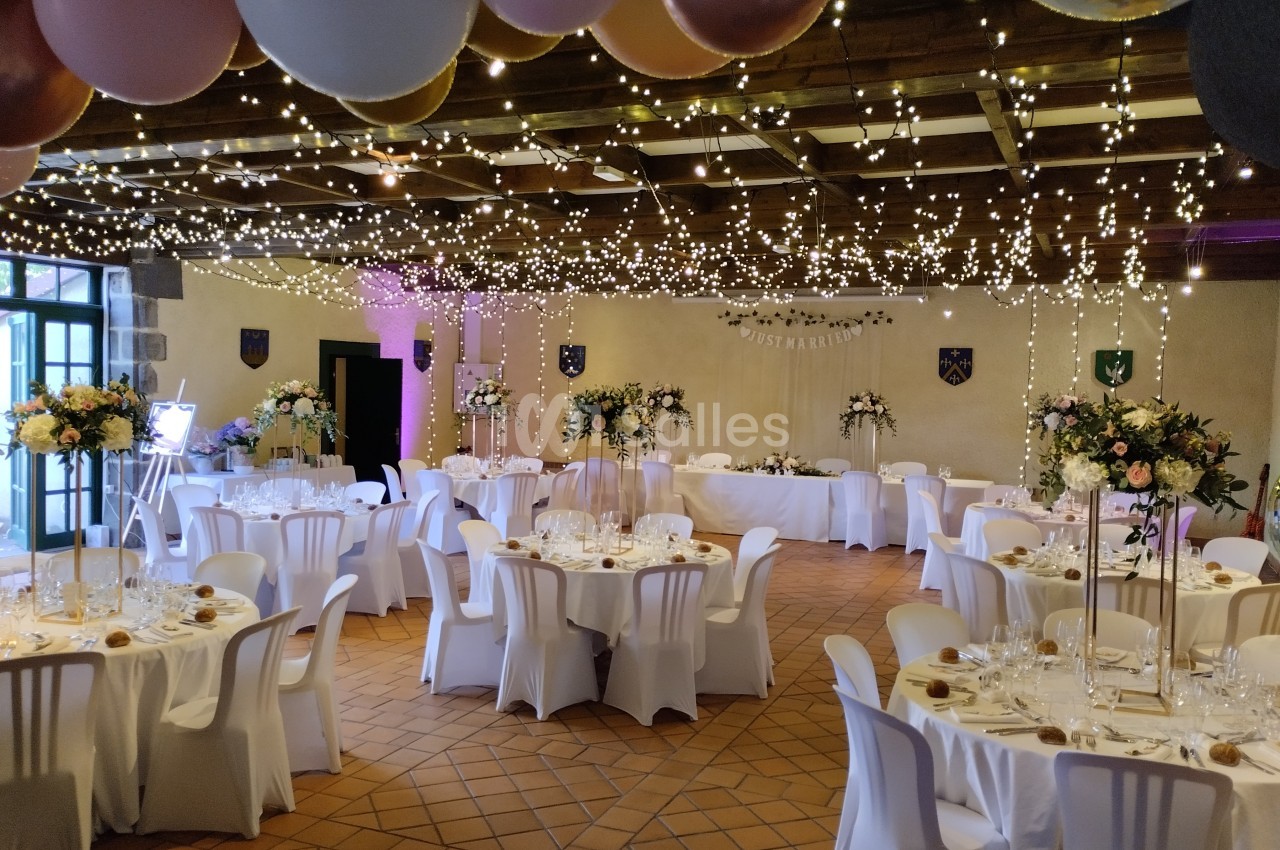 Salle de réception décorée pour un mariage, avec tables dressées, guirlandes lumineuses et ballons suspendus.