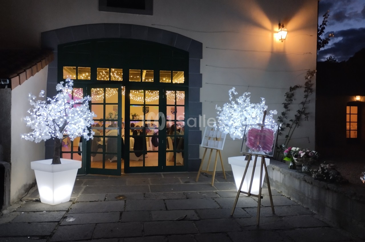 Entrée illuminée d'une salle de réception avec deux arbres décoratifs lumineux et une ambiance festive visible à l'intérieur.
