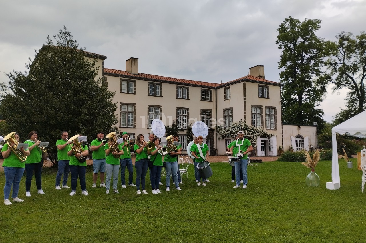 Un groupe de musiciens en tenue verte joue des instruments devant un grand bâtiment entouré de verdure.