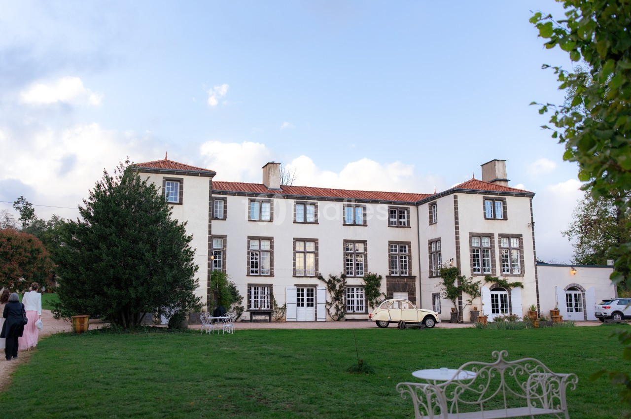 Façade d'un grand bâtiment blanc à trois étages avec un jardin verdoyant et une voiture ancienne stationnée devant.