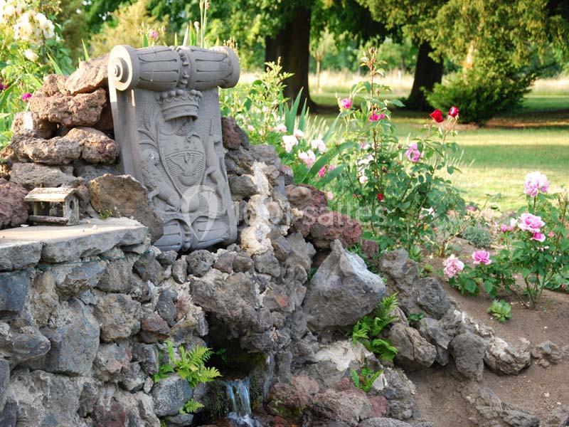 Statue en pierre sculptée entourée de rochers, fleurs colorées et verdure dans un jardin.