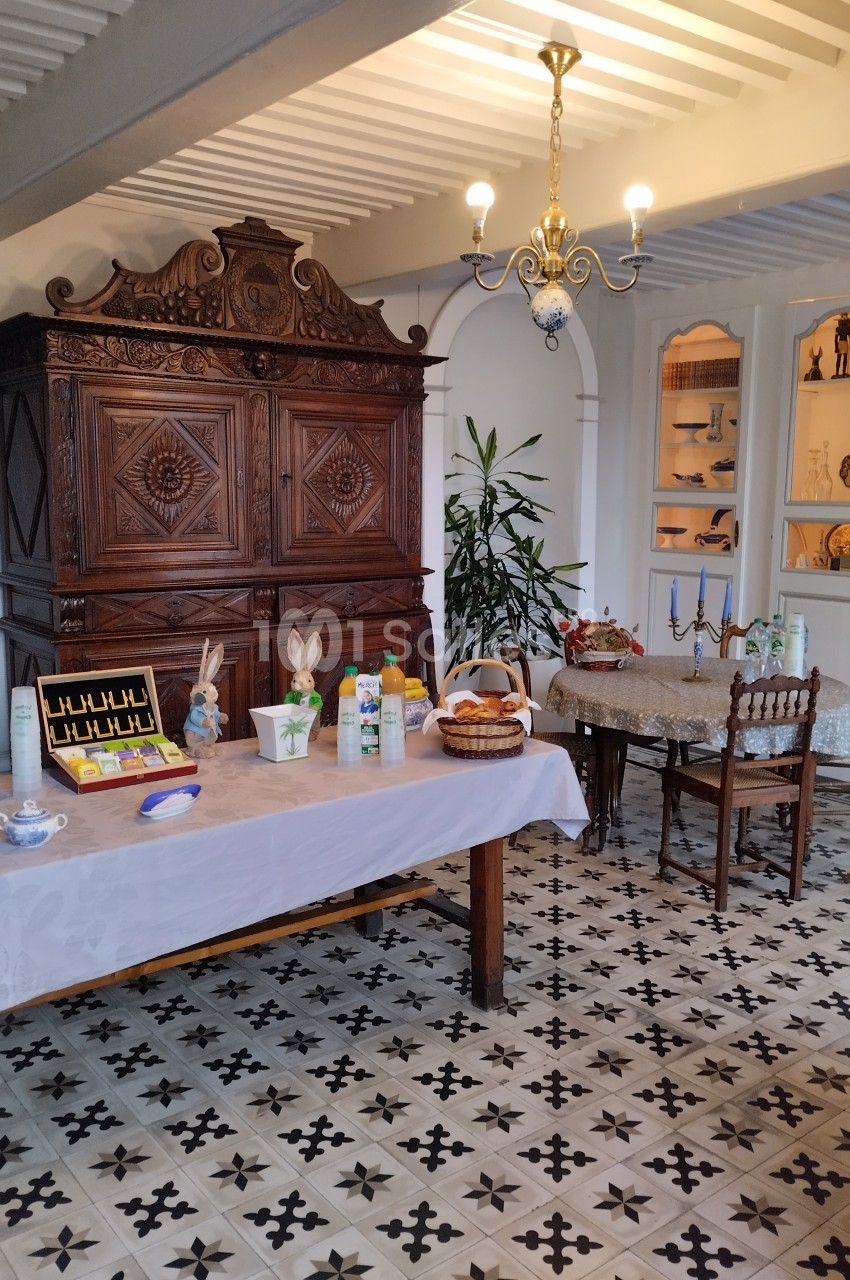 Salle à manger avec buffet ancien, table dressée pour un petit-déjeuner et sol en carreaux de ciment.