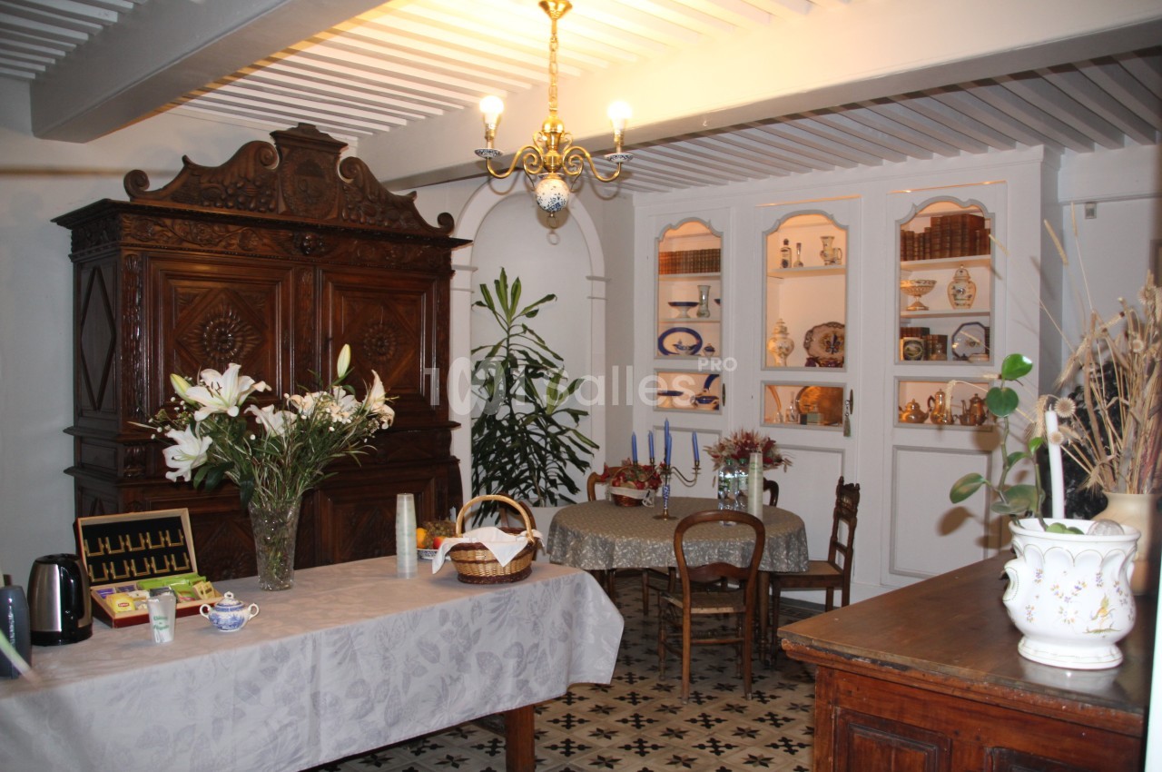 Salle à manger rustique avec meubles en bois, table dressée, fleurs, vaisselier et carrelage ancien au sol.