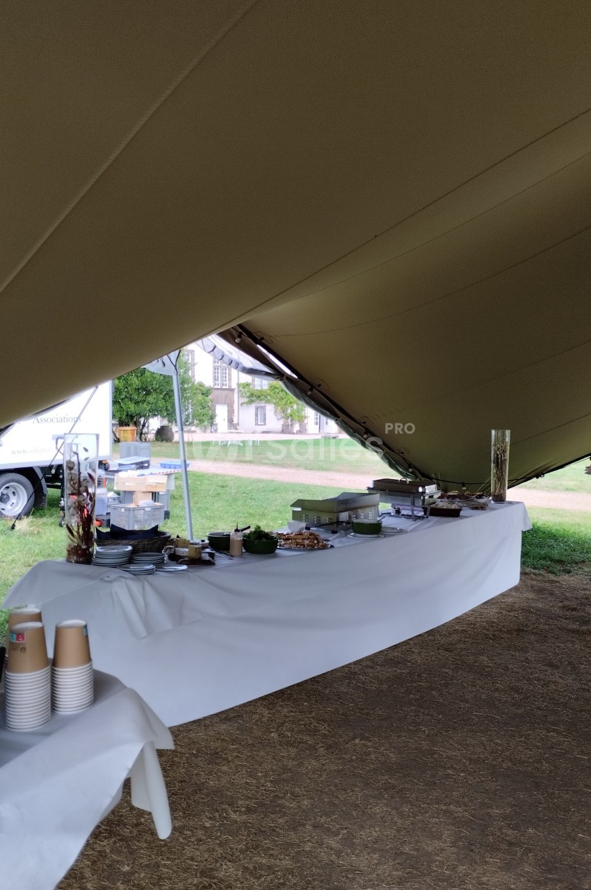 Table dressée sous une tente avec vaisselle, plats et boissons pour un buffet en extérieur.