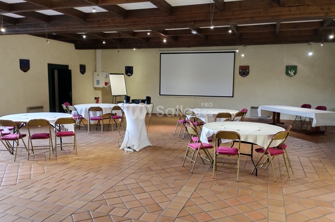 Salle de réunion avec tables rondes, chaises pliantes, vidéoprojecteur et écran, dans un espace au plafond en bois.