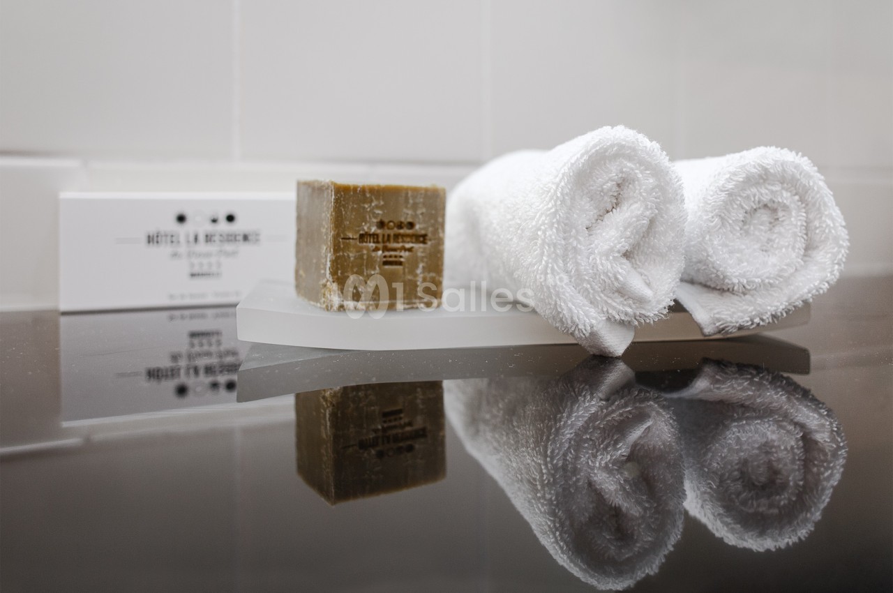 Deux serviettes blanches roulées, un savon et des articles de toilette disposés sur un plateau dans une salle de bain.
