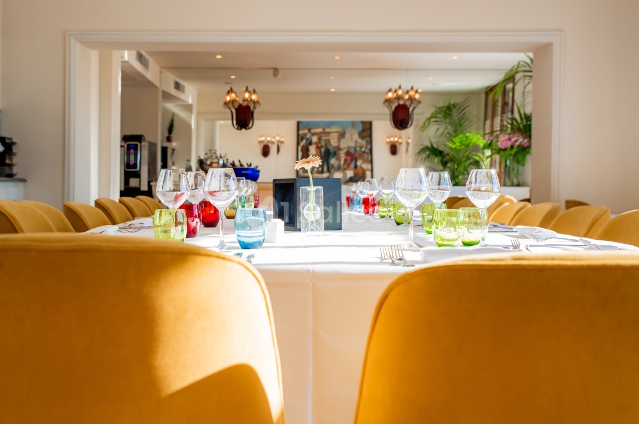 Table élégamment dressée avec des verres colorés et des chaises jaunes dans une salle lumineuse et décorée.