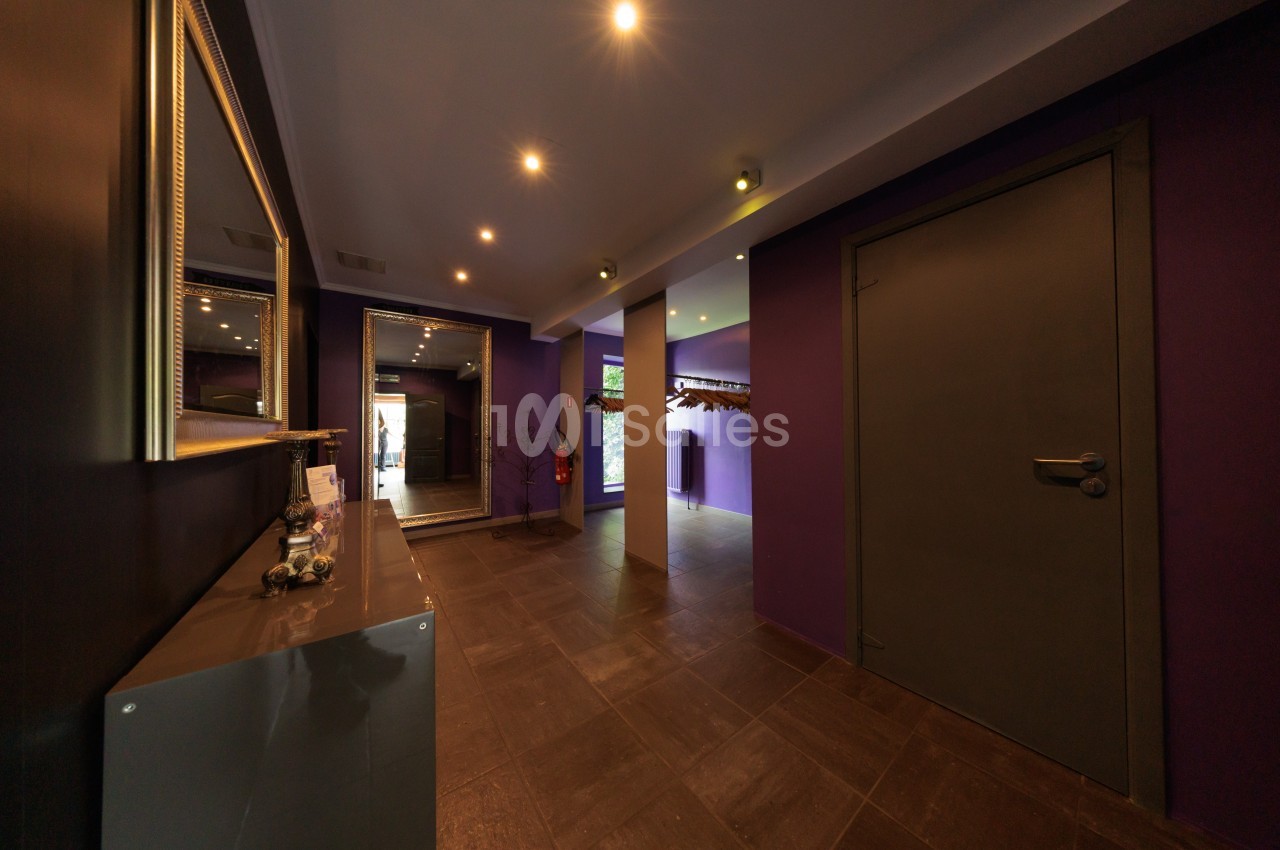 Couloir moderne avec murs violets, sol en carrelage foncé, éclairage encastré et porte fermée à droite.