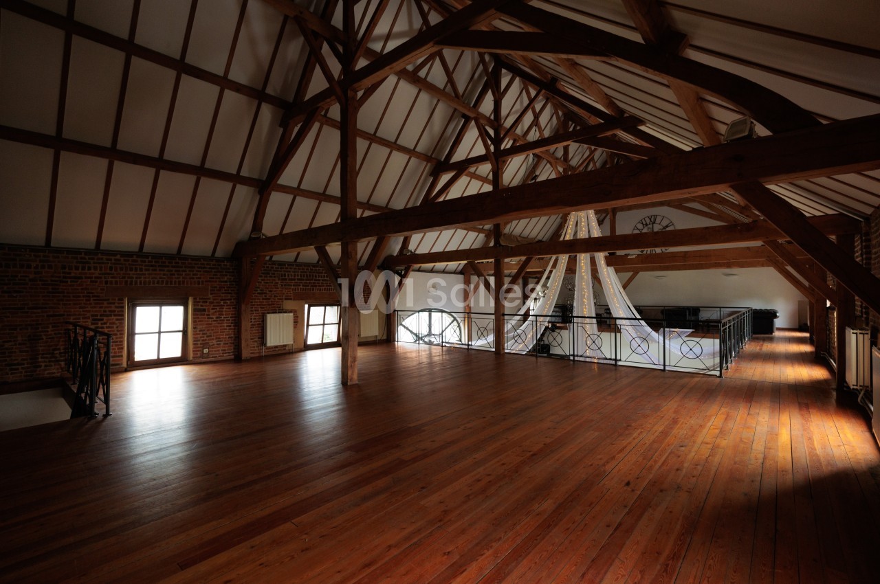 Intérieur d'un grand grenier rénové avec poutres apparentes, parquet en bois et lumière naturelle.