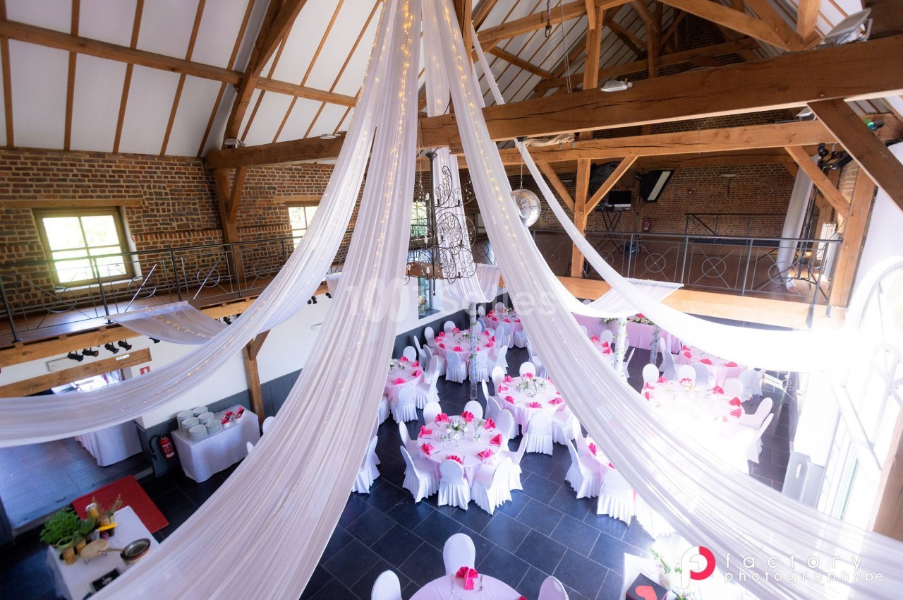 Salle de réception lumineuse avec des tables décorées de nappes blanches et des drapés suspendus au plafond.