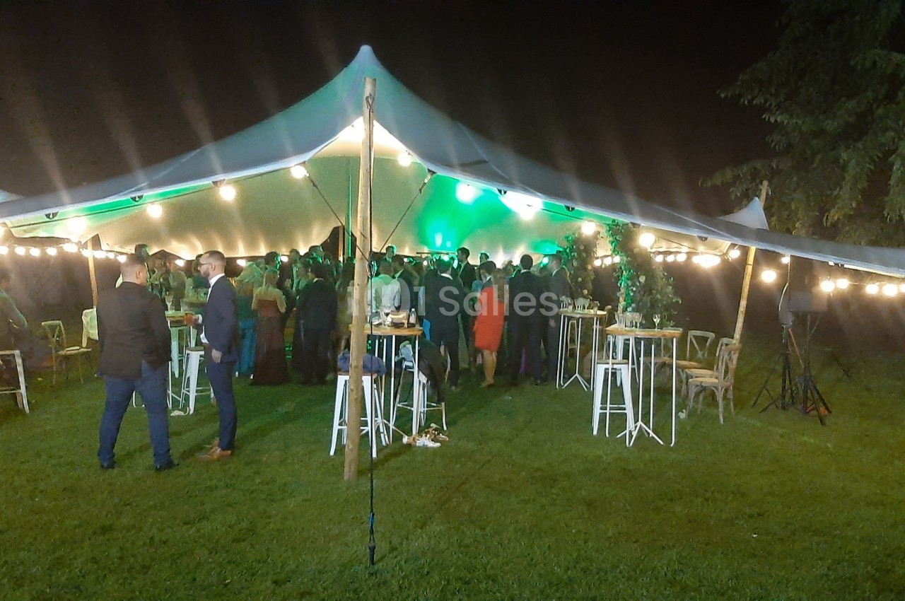 Tente éclairée accueillant un événement nocturne avec des invités debout autour de tables hautes sur une pelouse.