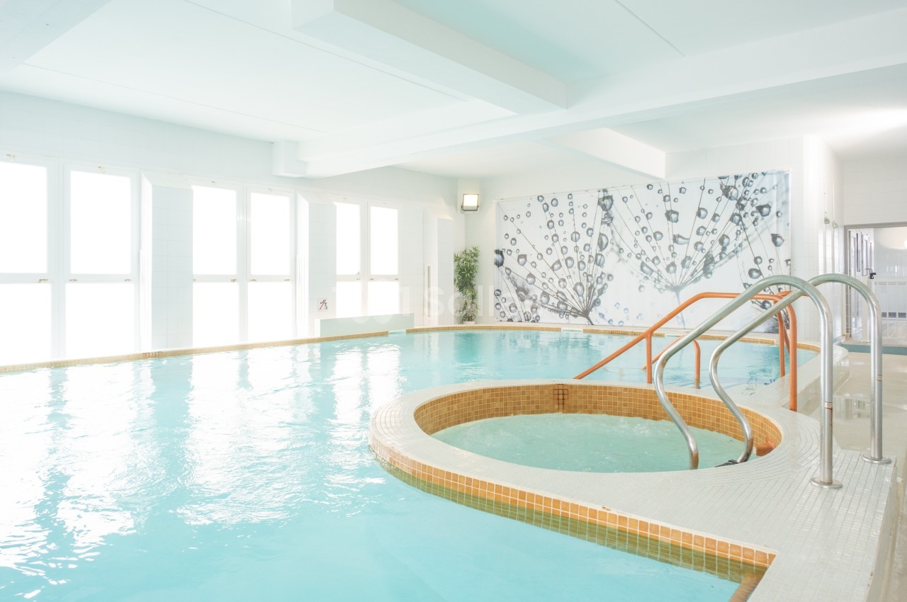Piscine intérieure lumineuse avec bassin rond intégré, entourée de murs blancs et décorée d'une fresque murale.