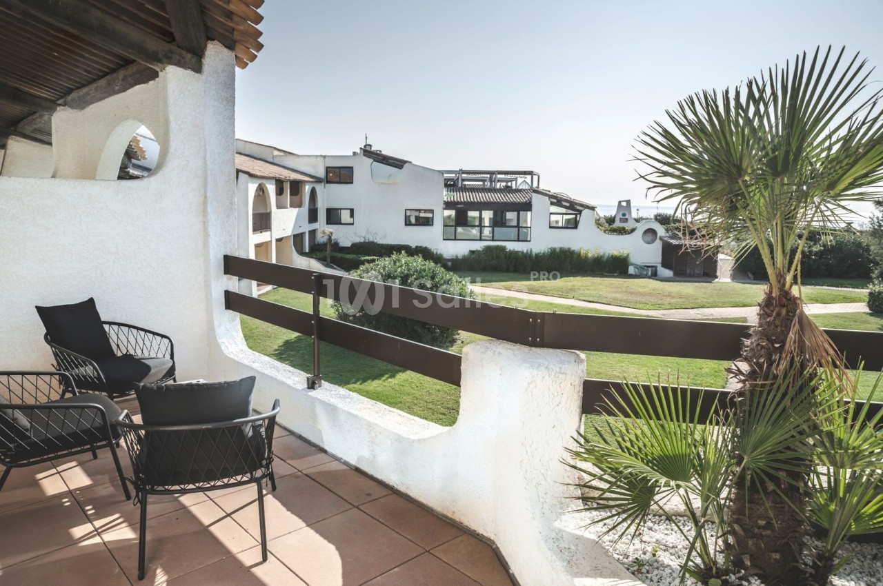 Terrasse avec mobilier en rotin noir, vue sur un jardin verdoyant et des bâtiments blancs au style méditerranéen.