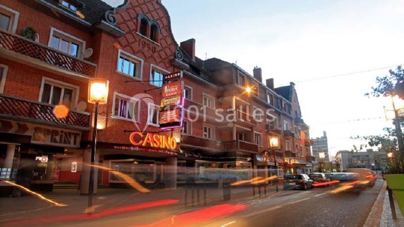 Façade d'un bâtiment en briques avec enseignes lumineuses, dont un casino, sur une rue animée en soirée.