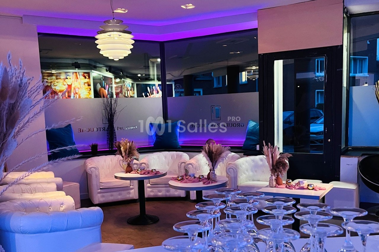 Salon moderne avec canapés blancs, tables basses décorées et éclairage violet, donnant sur une grande baie vitrée.