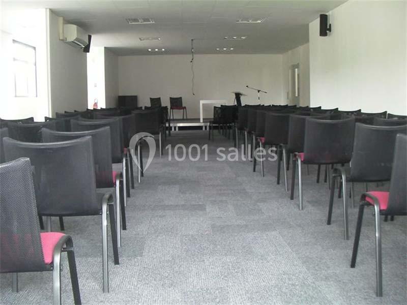 Salle de conférence vide avec des rangées de chaises noires et rouges, une estrade et un micro en arrière-plan.