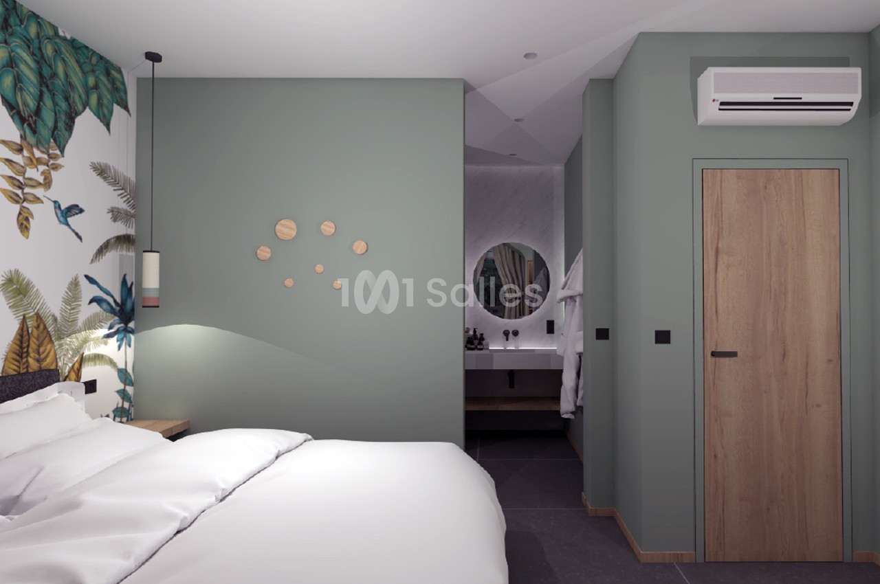 Chambre moderne avec lit, mur vert décoré, papier peint tropical et vue sur une salle de bain avec miroir rond.