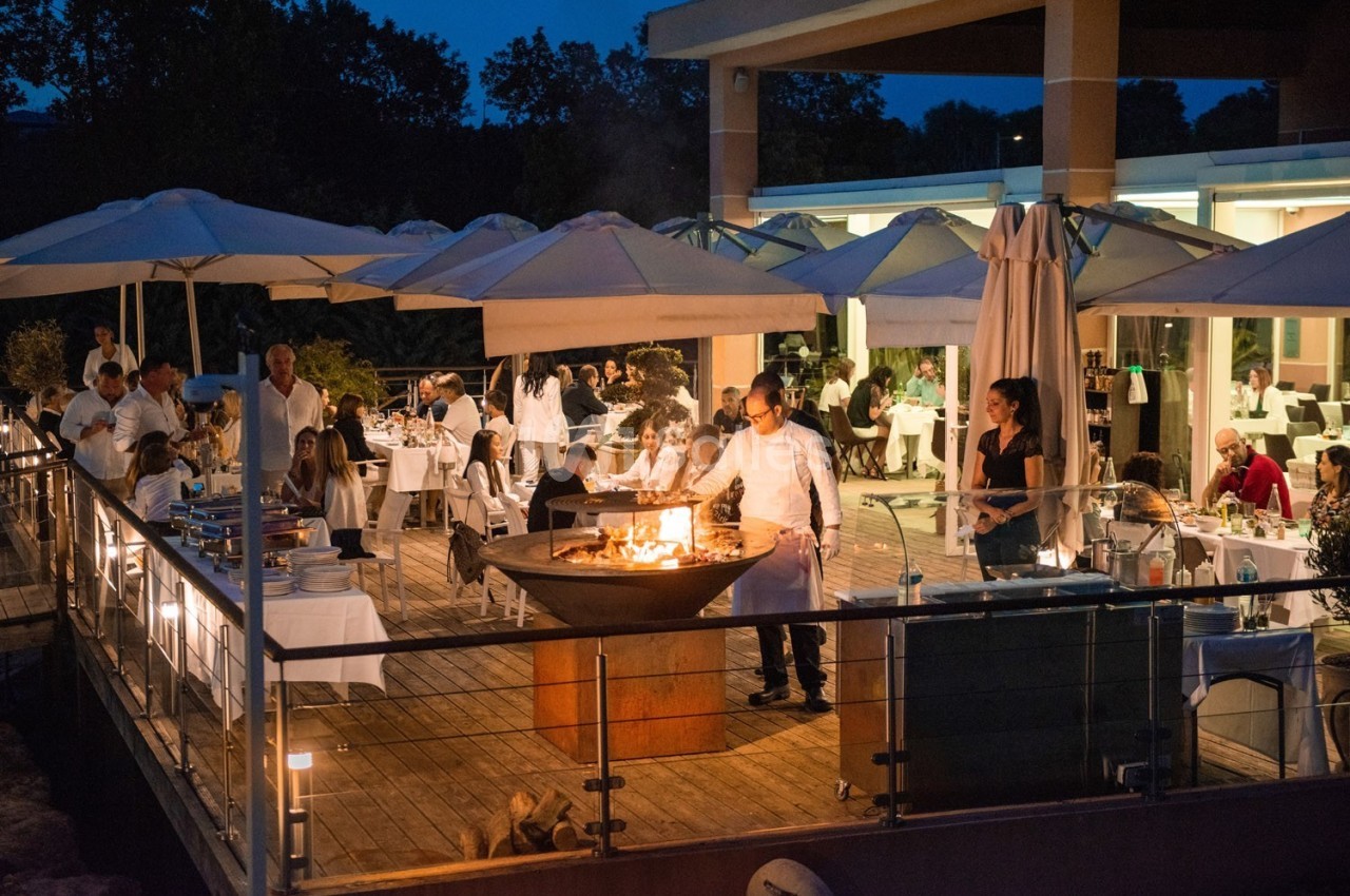 Terrasse d'un restaurant en soirée avec des convives attablés et un chef cuisinant sur un brasero.