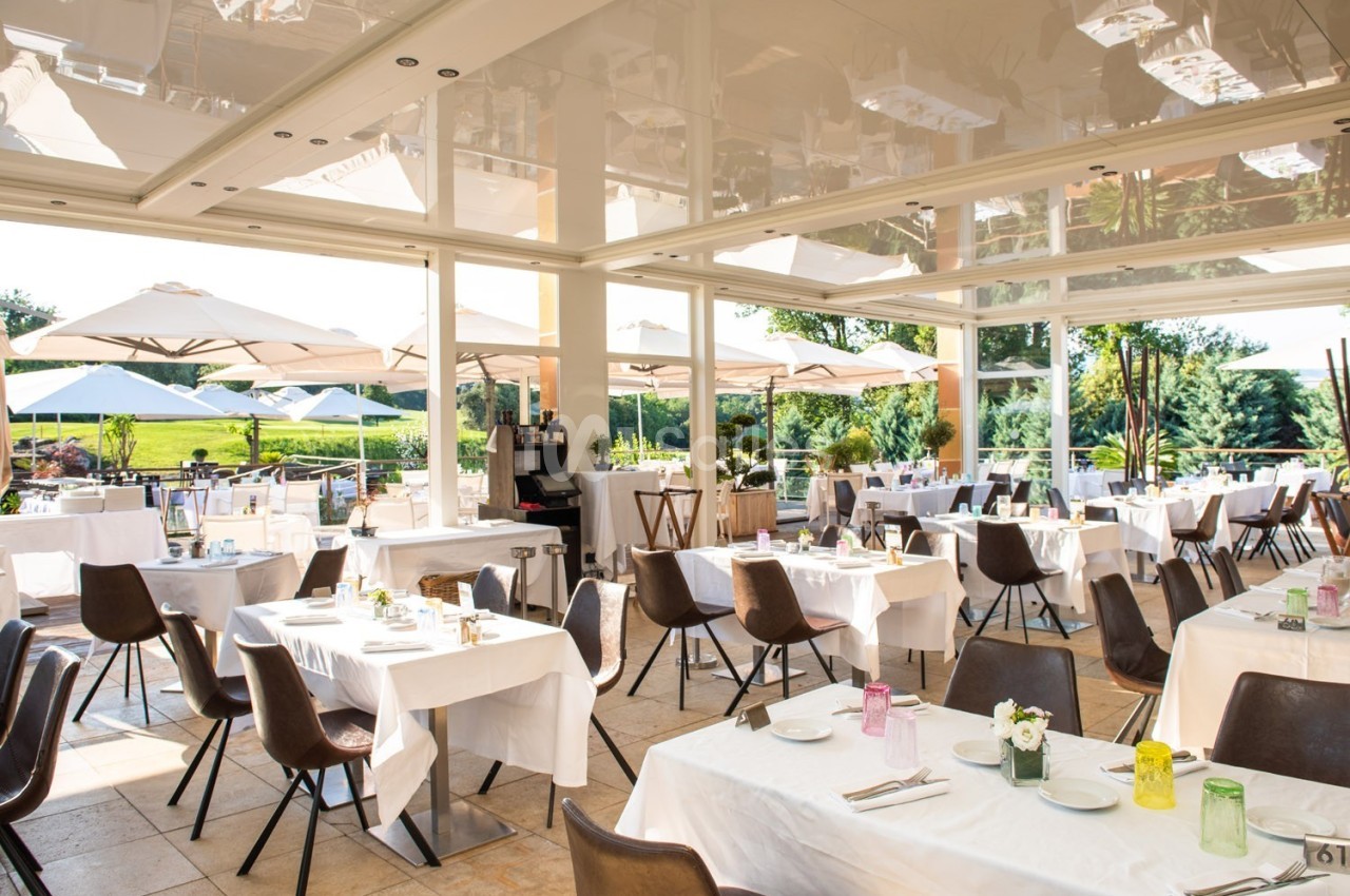 Salle de restaurant lumineuse avec tables dressées, grandes baies vitrées et terrasse extérieure avec parasols.