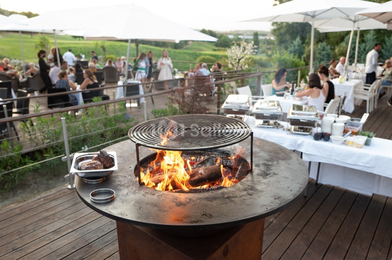 Barbecue en plein air sur une terrasse en bois, avec des convives assis à des tables sous des parasols.